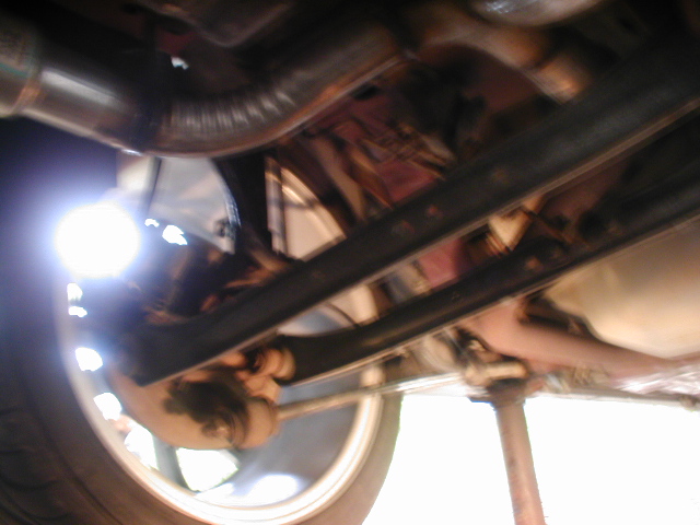 Underside view of a vehicle's exhaust system and wheel. Supermotors.net logo visible