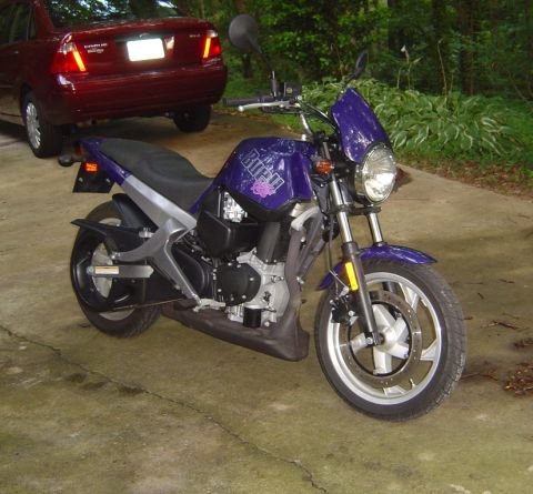 1986 Ford Bronco - A purple Buell motorcycle is parked on a concrete driveway next to a red sedan.