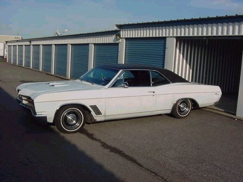 1986 Ford Bronco - White 1966 Buick Skylark coupe with a black vinyl roof parked outside storage units.