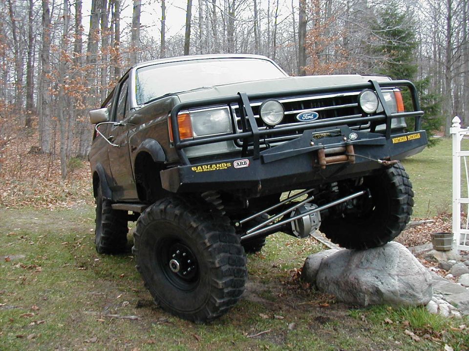 Lifted dark Ford Ranger on huge tires with brush guard and winch posed on a rock in the woods