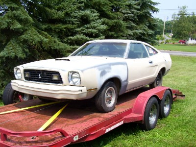 1978 Ford Mustang II - A white Ford Mustang II is being transported on a trailer, with primer visible on the front fender.