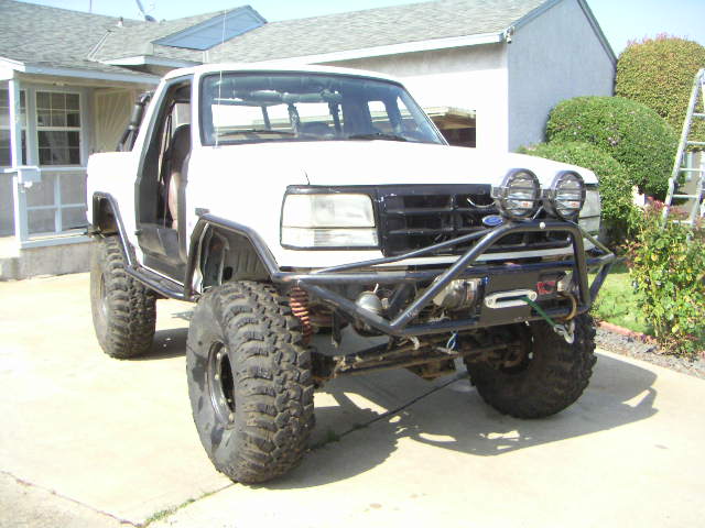 Lifted white Ford Bronco/pickup on big mud tires with tube bumper and winch in driveway