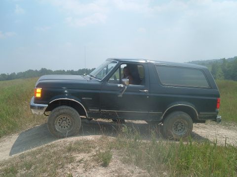1988 Ford Bronco - A dark blue Ford Bronco is shown driving off-road on a sunny day.
