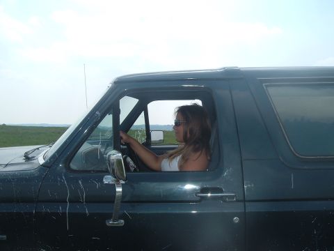 1988 Ford Bronco - Woman drives a dark green SUV with mud splatters on the side.