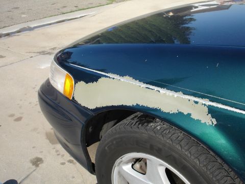 1995 Ford Taurus - The paint is peeling off the fender of a teal 1995 Ford Taurus, revealing primer underneath.
