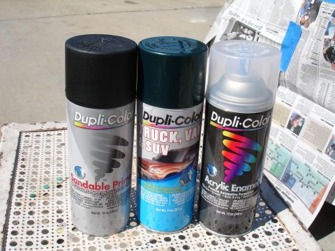 1995 Ford Taurus - Three cans of Dupli-Color spray paint are lined up on a metal table, with newspapers in the background.