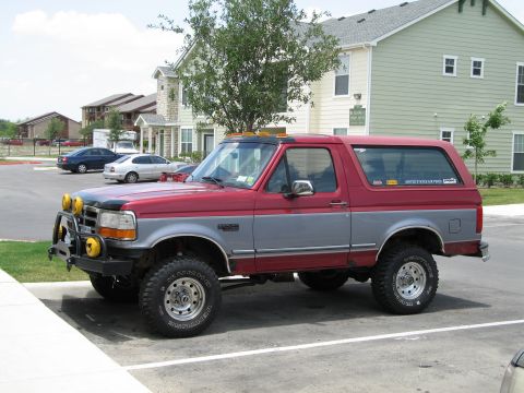 1995 Ford Bronco - A lifted Ford Bronco is parked in a lot with apartment buildings in the background.