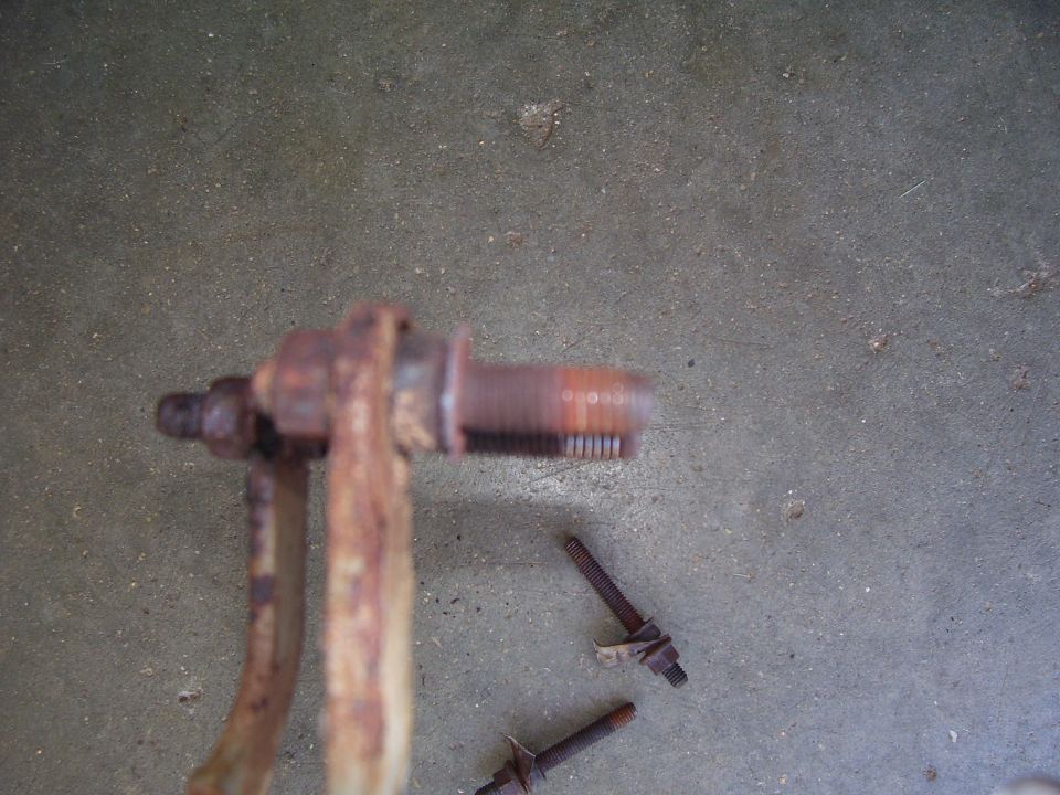 Rusty steering knuckle or spindle and two bolts lying on a concrete floor