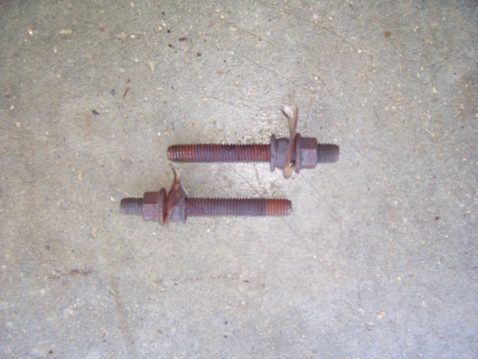 Two rusty studs with nuts and washers on a concrete floor