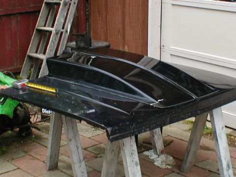 1998 Ford Taurus - A black car hood with a raised center section is displayed outdoors on sawhorses.