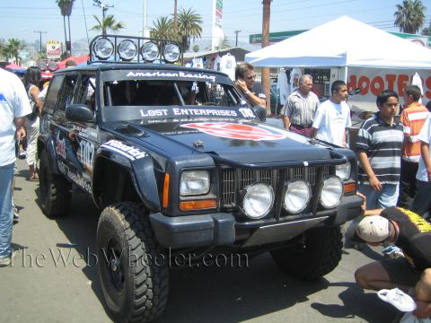 1990 Ford Bronco - black Jeep Cherokee off-road race vehicle with a roof light bar and Lost Enterprises decals sits among a crowd at an event.