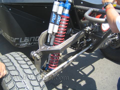 1990 Ford Bronco - Close-up of an off-road race vehicle's independent front suspension showing a red coilover spring and twin blue Fox shocks.