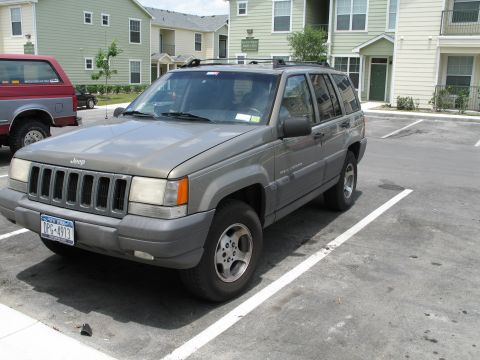 1995 Ford Bronco - A gray Jeep Grand Cherokee is parked in a lot next to a red pickup truck.