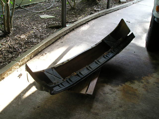 Curved metal bumper assembly with mounting brackets lying on a driveway
