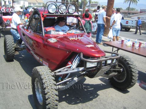 1990 Ford Bronco - red mid-engine tube-chassis off-road race buggy with a roof light bar sits on a street as spectators gather around it.