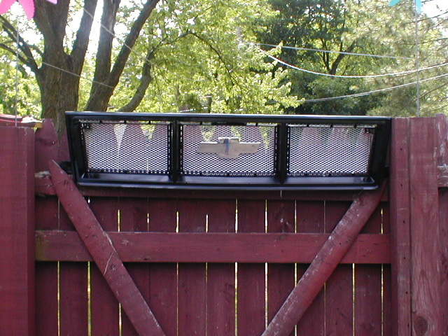 Black steel mesh truck headache rack mounted on a red wooden fence in a backyard