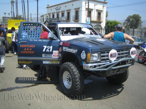 1990 Ford Bronco - blue Chevrolet S-10 number 721 prerunner with Ventura 4x4 Center and Sirius decals sits on a street before a stone building.