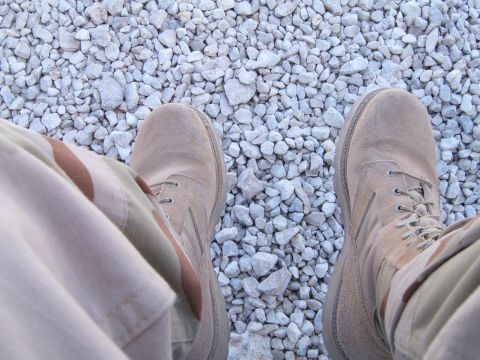 1988 Ford Bronco - View from above of someone in desert boots and camouflage pants standing on a surface of small rocks.