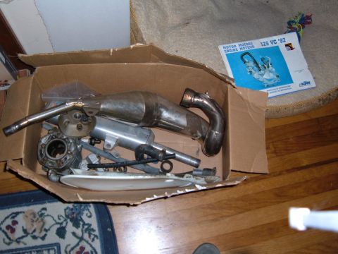 1985 Ford Bronco II - Cardboard box filled with motorcycle exhaust and engine parts, alongside a KTM 125 VC '92 manual.