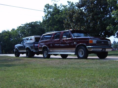 1993 Ford Bronco - Two Ford Broncos are parked on a paved surface with grass and trees in the background.