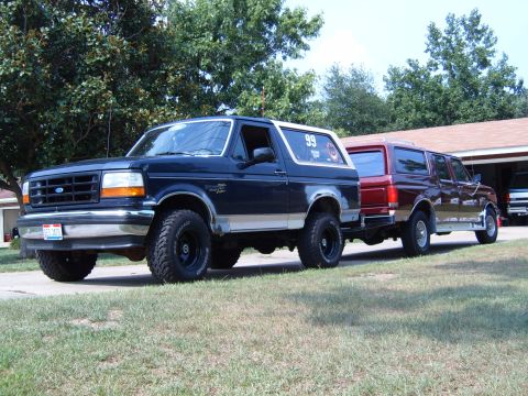 1993 Ford Bronco - A dark blue Ford Bronco tows a red Ford Econoline van in front of a garage.