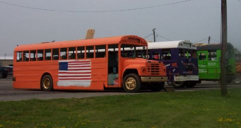 1978 Ford Bronco - Multiple converted school buses are parked in a lot under an overcast sky.