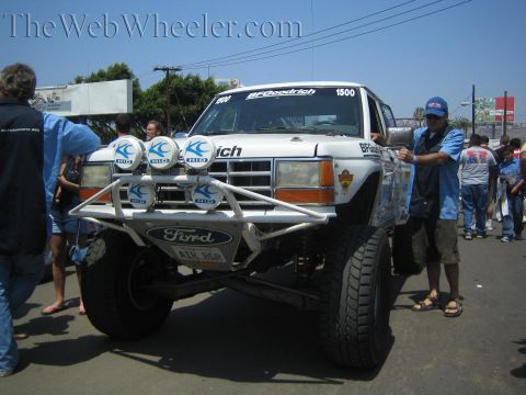 1990 Ford Bronco - Front view of a white Ford off-road prerunner truck numbered 1500 with a roof light bar and BFGoodrich livery, surrounded by spectators.