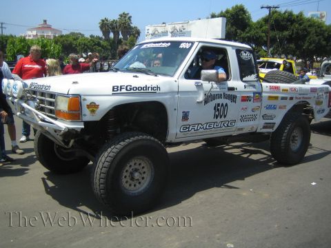1990 Ford Bronco - Side-front view of a white Ford race truck number 1500 lettered Airborne Ranger and Camburg, with a roof light pod and a crowd nearby.