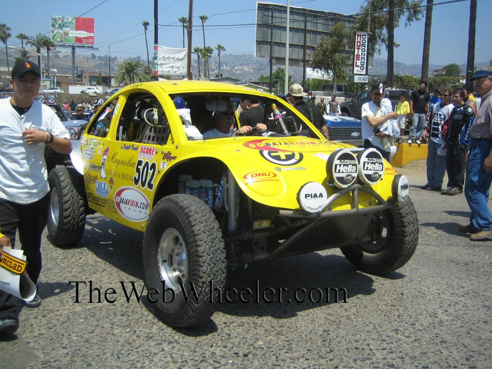 Yellow Baja Bug race car no. 502 with sponsor decals, three-quarter front view
