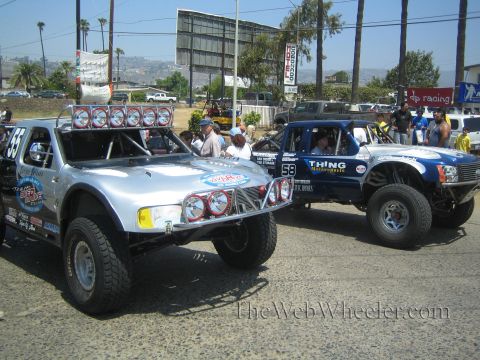 1990 Ford Bronco - silver off-road buggy numbered 55 and a blue Toyota prerunner truck numbered 58 lettered Thing Motorsports parked beside each other.