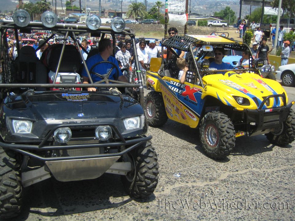 Black Polaris UTV and yellow side-by-side with roof lights parked among a crowd