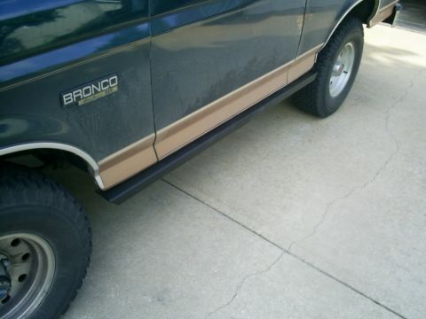 1994 Ford Bronco - Side view of a dark green and tan Ford Bronco, showing its black step bars and chrome trim.