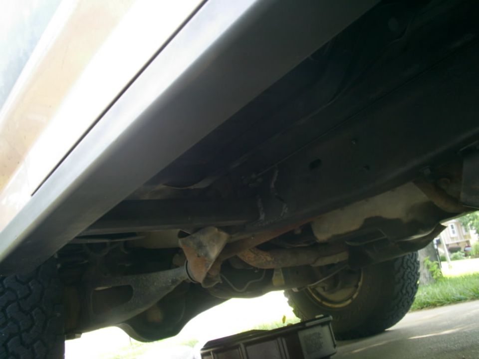Underside of a vehicle showing the frame, exhaust, and tire