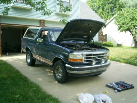 1994 Ford Bronco - A dark blue 1994 Ford Bronco sits in a driveway with its hood open, revealing the engine compartment.