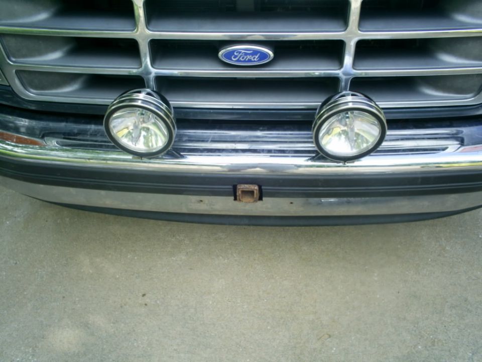 1994 Ford Bronco front grille with Ford emblem and two auxiliary lights mounted above chrome bumper with tow hitch receiver