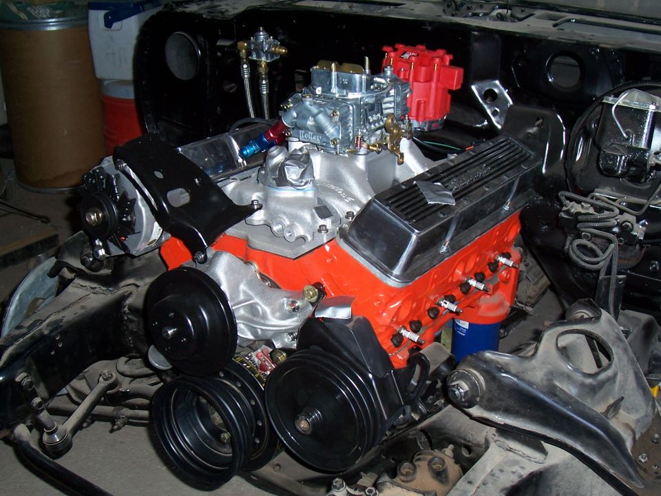 Orange small-block Chevy with Holley carb, red HEI cap and chrome valve covers in engine bay