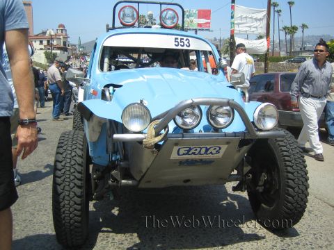 1990 Ford Bronco - Front view of a light blue VW Beetle-based Baja race car numbered 553 with twin round lights and a roof light pod, spectators alongside.