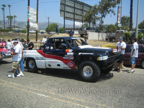 1990 Ford Bronco - Side view of a black, red and white off-road race truck with Yokohama and sponsor decals parked on a street, spectators nearby.