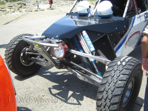 1990 Ford Bronco - Close-up of the front suspension of a silver and blue off-road buggy showing tube A-arms, coilover shocks and an all-terrain tire.