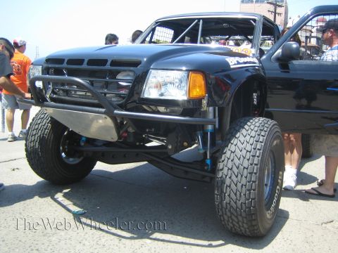 1990 Ford Bronco - Front view of a black Ford Ranger off-road prerunner with a tube front bumper, blue bypass shocks and BFGoodrich tires, spectators around i…