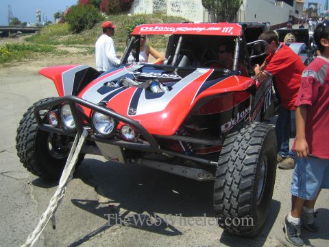 1990 Ford Bronco - red and black single-seat off-road race buggy marked 117 with DeJong Racing graphics sits among spectators on pavement.