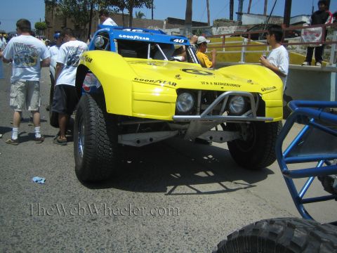 1990 Ford Bronco - bright yellow tube-frame off-road race buggy number 40 with Goodyear graphics is surrounded by crew in a staging area.