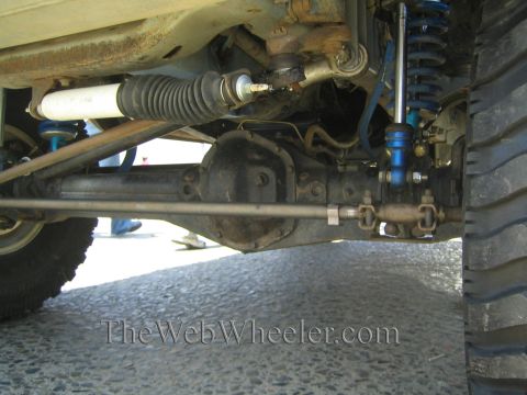1990 Ford Bronco - Close-up underside view of a lifted truck's front suspension with a steering rack, blue coilover shock, and tie rods.