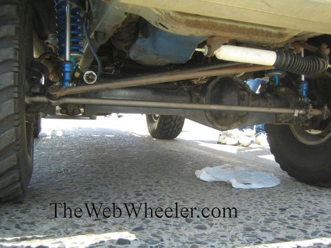 1990 Ford Bronco - Underside view of a lifted truck's front suspension with a solid axle, blue coilover shocks and drag link over pavement.