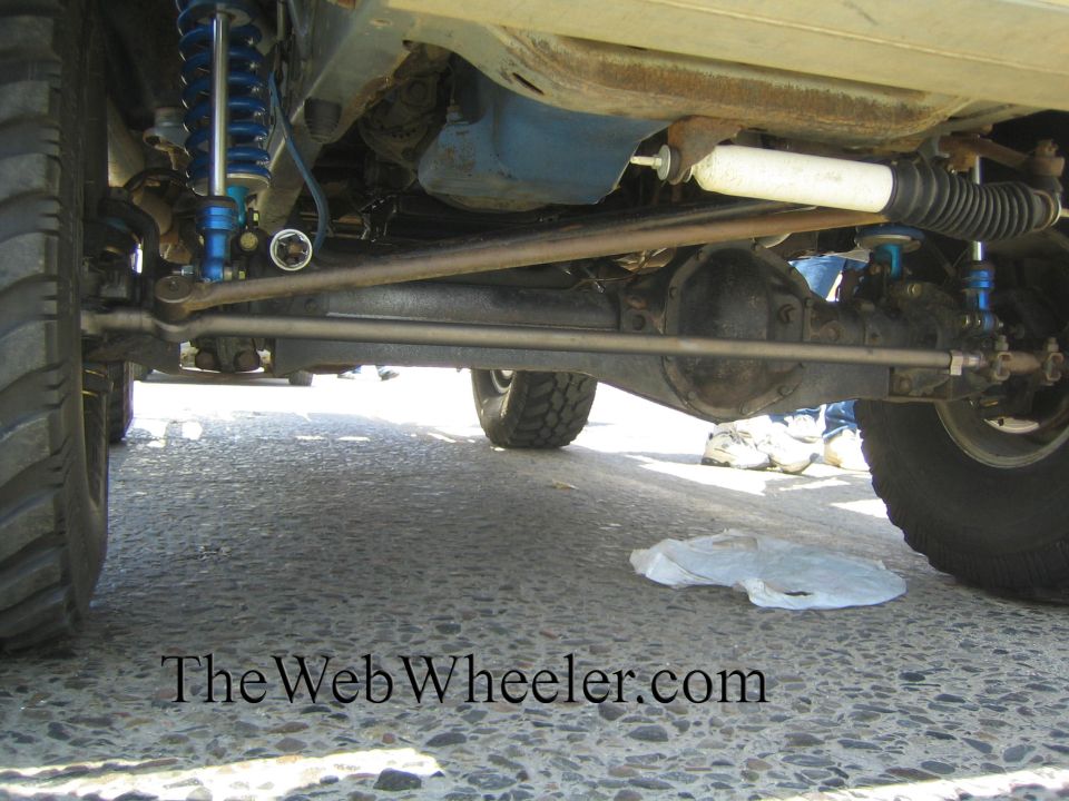 Underside of a lifted truck showing solid axle, blue shocks, and steering linkage