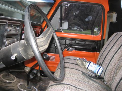 1979 Ford Bronco - The interior of a 1979 Ford Bronco features an orange dashboard and door panels, a large steering wheel, and patterned fabric seats.