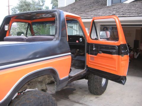 1979 Ford Bronco - The interior of an orange and black Ford Bronco, viewed from the side with the doors open.