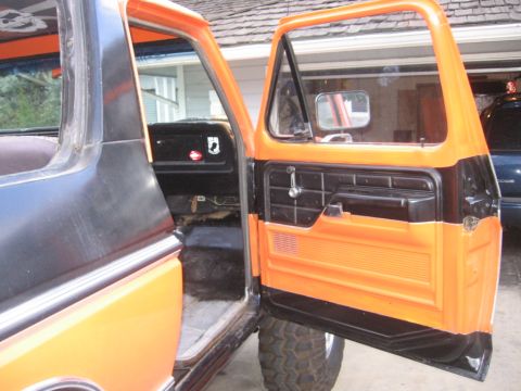 1979 Ford Bronco - The interior door panel features a two-tone orange and black design with a chrome handle and speaker grille.