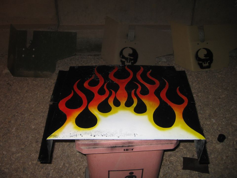 Black car part with airbrushed red and yellow flames and two skull decals on adjacent parts