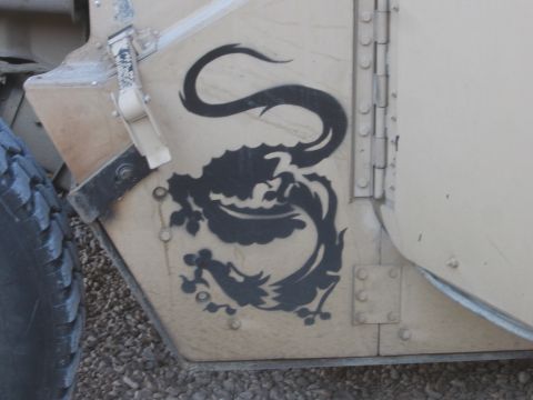 1979 Ford Bronco - A black dragon graphic is stenciled on the side of a tan military vehicle, with a tire visible on the left.